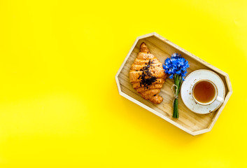 Wall Mural - Breakfast with summer flowers. Tea, croissant and cornflowers on yellow background top-down copy space