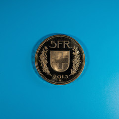 five-franc Swiss coin lies against a blue background.