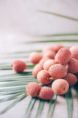 Wall Mural - Lychee fruits with palm leaves on rattan background. Copy space. Exotic litchi, lichee fruits. Tropical food concept.