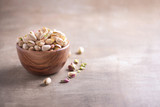 Fototapeta  - Green pistachio nuts in wooden bowl on wood textured background. Copy space. Superfood, vegan, vegetarian food concept. Macro of pistachio nut texture, selective focus. Healthy snack.
