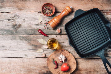 Wall Mural - Cast iron pan, spices, pepper shaker, meat fork, oil, spices on wooden background. Top view. Copy space. Healthy, clean food and eating concept. Zero waste. Cooking ingredients frame