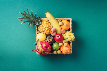 Tropical fruits on green background. Rattan box full of exotic thailand fruits - pineapple, pitahaya, kiwano, african horned melon, tamarillo fruit, granadilla, feijoa, salak, snake fruits, maracuya