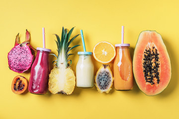 Wall Mural - Detox summer drink. Vegan, vegetarian, fructorian diet. Fresh smoothie and juicy fruits - papaya, orange, pineapple, dragon fruit, pitahaya, tamarillo fruit over yellow background. Top view, flat lay