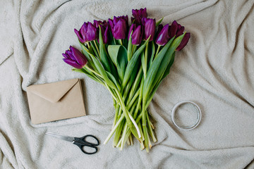 Spring flowers, bunch of purple tulips and envelope on beige plaid, envelope of craft paper, scissors and tape flat lay.