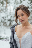 Fototapeta Do akwarium - a beautiful girl in a wedding dress stands in a winter pine forest