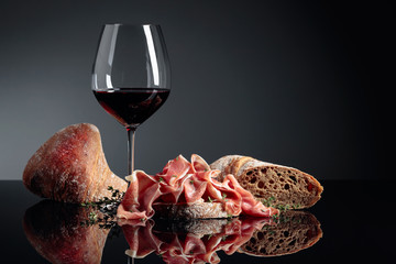 Wall Mural - Prosciutto with ciabatta, red wine and thyme on a black background.