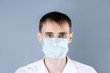 © borislav15 - Man in a medical mask. A handsome dark-haired, brown-eyed man in a white shirt and medical mask  ,dressing gown looking at camera , on a gray background. Chinese Coronavirus , Covid-19
