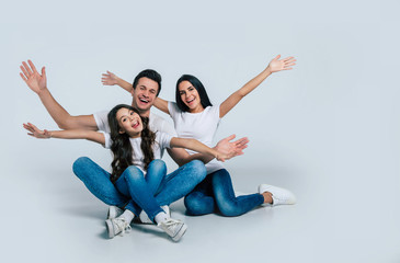 Beautiful excited and the funny family team is posing and pointing in a white t-shirt while they isolated on white background in studio.