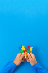 Wall Mural - World autism awareness day concept. Child hands holding colorful puzzle heart on blue background