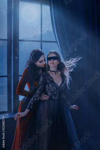 Fotografía Wicked insidious medieval witch red long velvet dress seduces cute beautiful princess in black mask