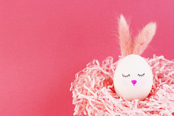 Easter egg of a rabbit on a pink background. an egg with a cute face and pink ears. Rabbit girl in the nest. a nest of decorative paper