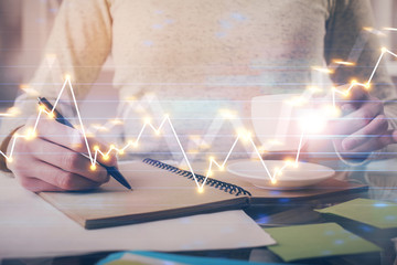 Forex chart hologram on hand taking notes background. Concept of analysis. Double exposure