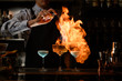 © fesenko - bartender makes fire over several glasses with cocktails