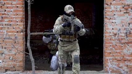 Wall Mural - Two military men in white camouflage and green uniform, in winter forest. Soldiers with machinegun go out from broken building. front view.