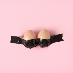 Poster - Creative Easter concept with eggs and duct tape on pastel pink and background. Minimal Easter Holiday idea. Woman's breasts made with Easter eggs.