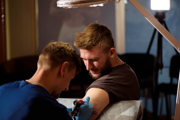 Tattoo artist makes a tattoo on a man's hand.