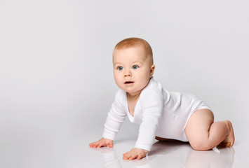 Wall Mural - Chubby ginger little one in bodysuit, barefoot. He is sitting on floor isolated on white studio background. Close up, copy space