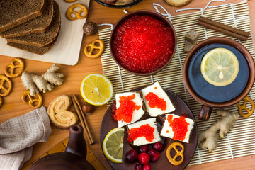 Sandwiches with butter and red caviar are on the plate. Next to it is a Cup of tea with lemon.