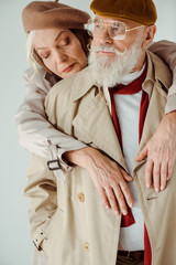 Stylish senior woman embracing handsome man isolated on grey