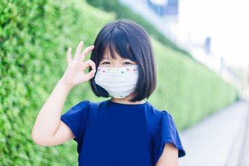 Coronavirus and Air pollution pm2.5 concept.Little chinese girl wearing mask for protect pm2.5 and pointing finger in mask for corona virus protection.Covid-19 coronavirus and pandemic virus symptoms.