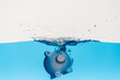 piggy bank going under blue water with splash isolated on white, coronavirus crisis concept
