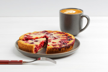 Homemade berry pie with yogurt filling and cup of coffee cappuccino on white wooden table