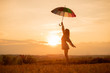 Young woman with umbrella standing in field at sunset
