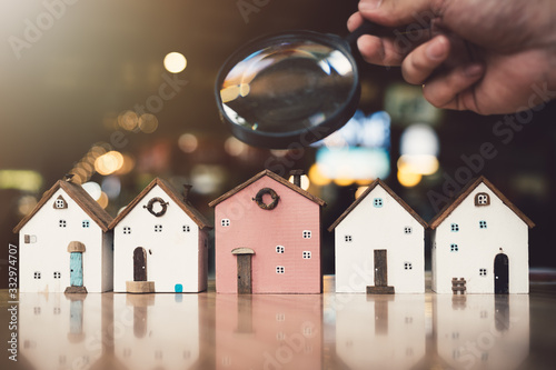 Fotomural Hand holding magnifying glass and looking at house model, house selection, real estate concept