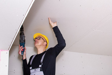 A builder standing on a ladder installs drywall at a construction site