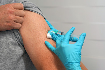 Doctor vaccinates a man. Doctor or nurse hands with syringe doing injection of vaccine to male patient. Female doctor vaccinates a man. Vaccination concept.