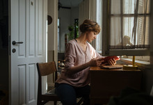 Young Woman Reading Book At Table At Home
