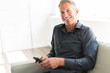 © Louis-Paul Photo - Portrait of mature man relaxing at home in sofa and cellphone