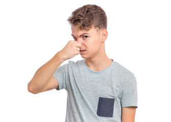 Wall Mural - Teen boy with gesture smells bad. Child covers nose with hand, smells something awful, pinches nose, frowns in displeasure. Teenager showing that something stinks, isolated on white background.