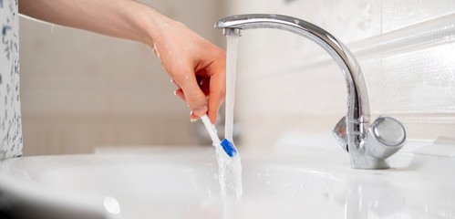 a close up hand holding a white toothbrush and wash it under the water in sink in bathroom