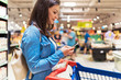 © Santi Nunez/Stocksy - Beautiful woman using mobile phone in a supermarket