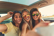 Three female friends enjoying traveling in the car. Sitting in rear seat and and making selfie.