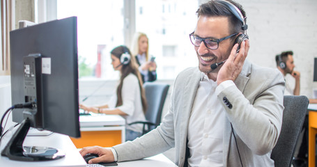 Wall Mural - Confident male customer support operator with headset working in call center