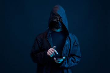 Dangerous hooded hacker with smartphone in his hand. Internet, cyber crime, cyber attack, system breaking and malware concept. Anonymous. Dark background.