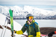 © Cavan Images - A man with backpack, radio, and skis with mountains behind him