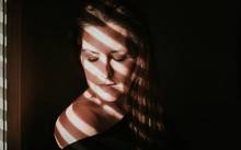 Portrait Of Woman Beside A Window With Shadows Across Her Face.