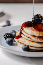 Close Up Of Syrup Pouring Down A Stack Of Pancakes With Berries On Top