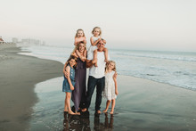 Traditional Portrait Of Family With Four Children Smiling At Beach Sun
