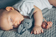 Sweet newborn baby sleeps with a gray toy hare on gray blanke