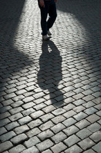 Shadow Figure Of Unrecognizable Person Walking On Dark Cobblestone Street
