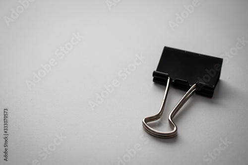 Fotomural black binder clip paper clip on white paper background in the top right corner w