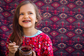 Cute happy young smiling girl eat homemade sweet chocolate paste spread from big glass jar with joy and pleasure