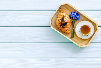 Wall Mural - Breakfast with summer flowers. Tea, croissant and cornflowers on blue wooden background top-down copy space