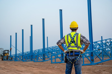 Poster - Construction worker wearing safety harness working in a metal roof structure at construction site.