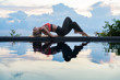 © mizuno555 - Young woman with long hair doing yoga early morning outdoor by the pool with sea view