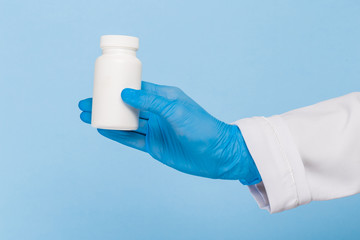 Doctor's hands in sterile gloves hold a jar of pills on a blue background. Infection control concept.